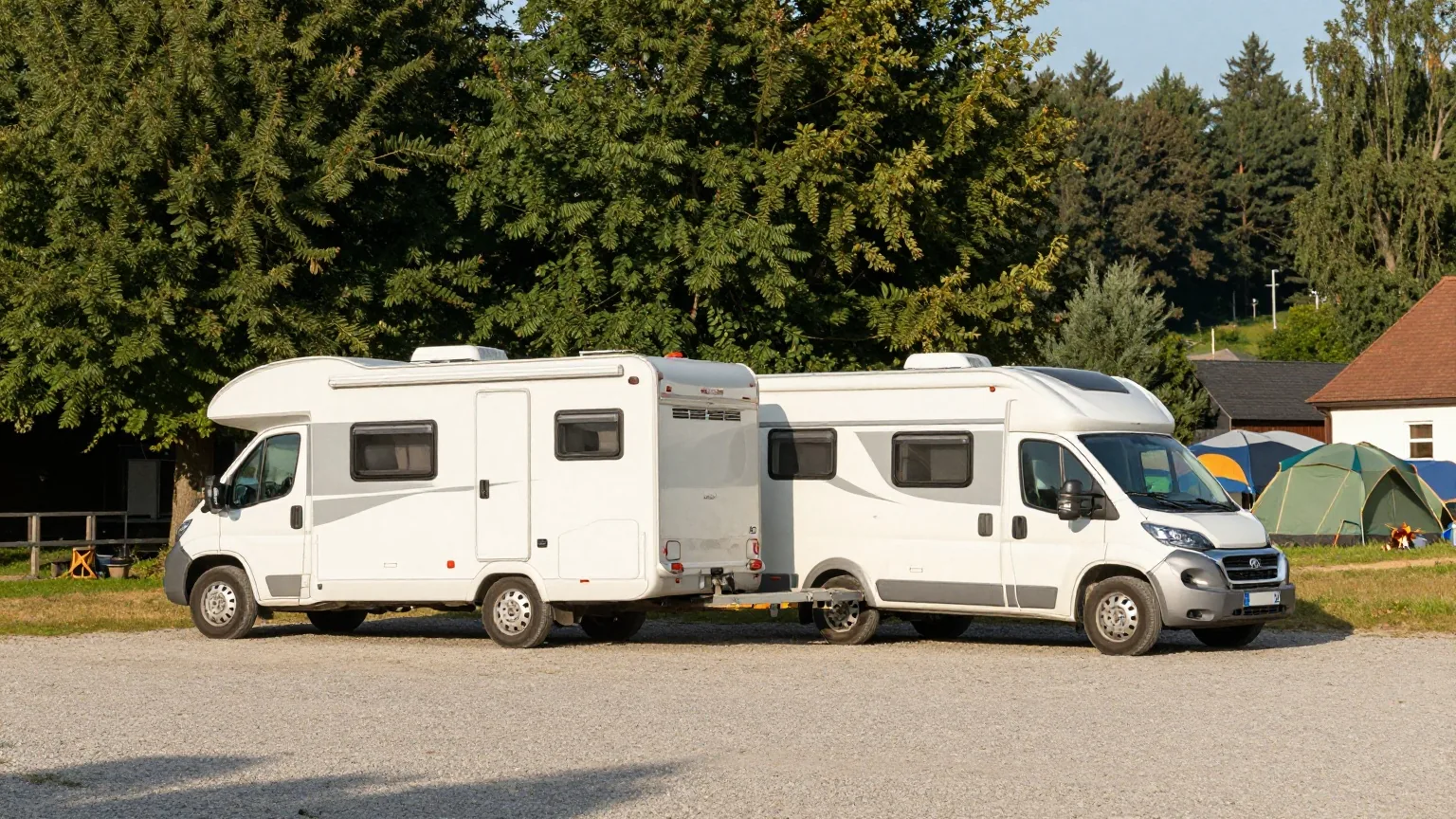 Ein weißes Wohnmobil und ein Auto mit kleinem Wohnwagen stehen nebeneinander auf einem Kiesplatz am Rand eines Campingplatzes
