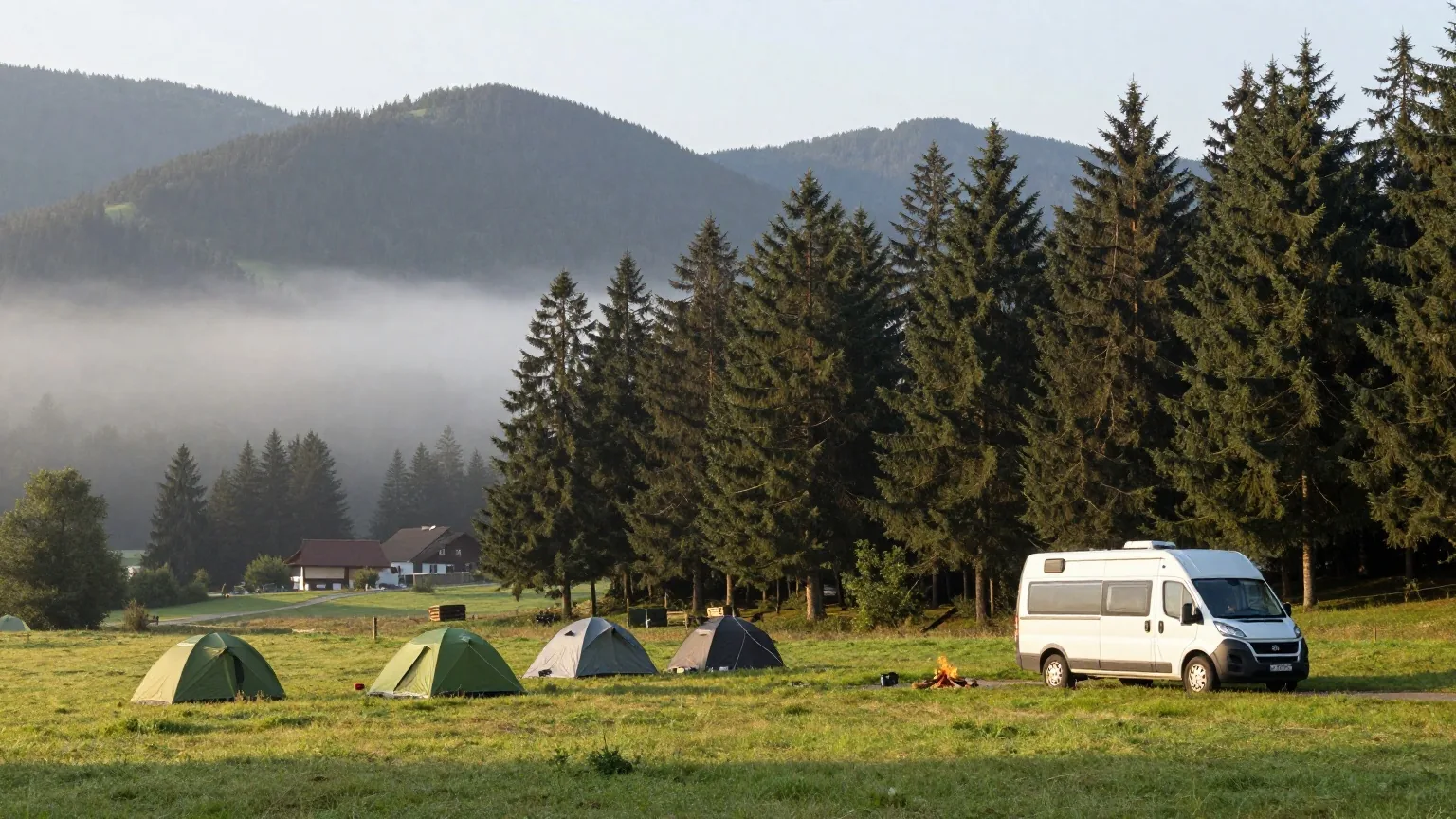 Ein ruhiger Campingplatz am Rand eines Fichtenwaldes im Mittelgebirge, Zelte und ein weißes Wohnmobil im Morgennebel